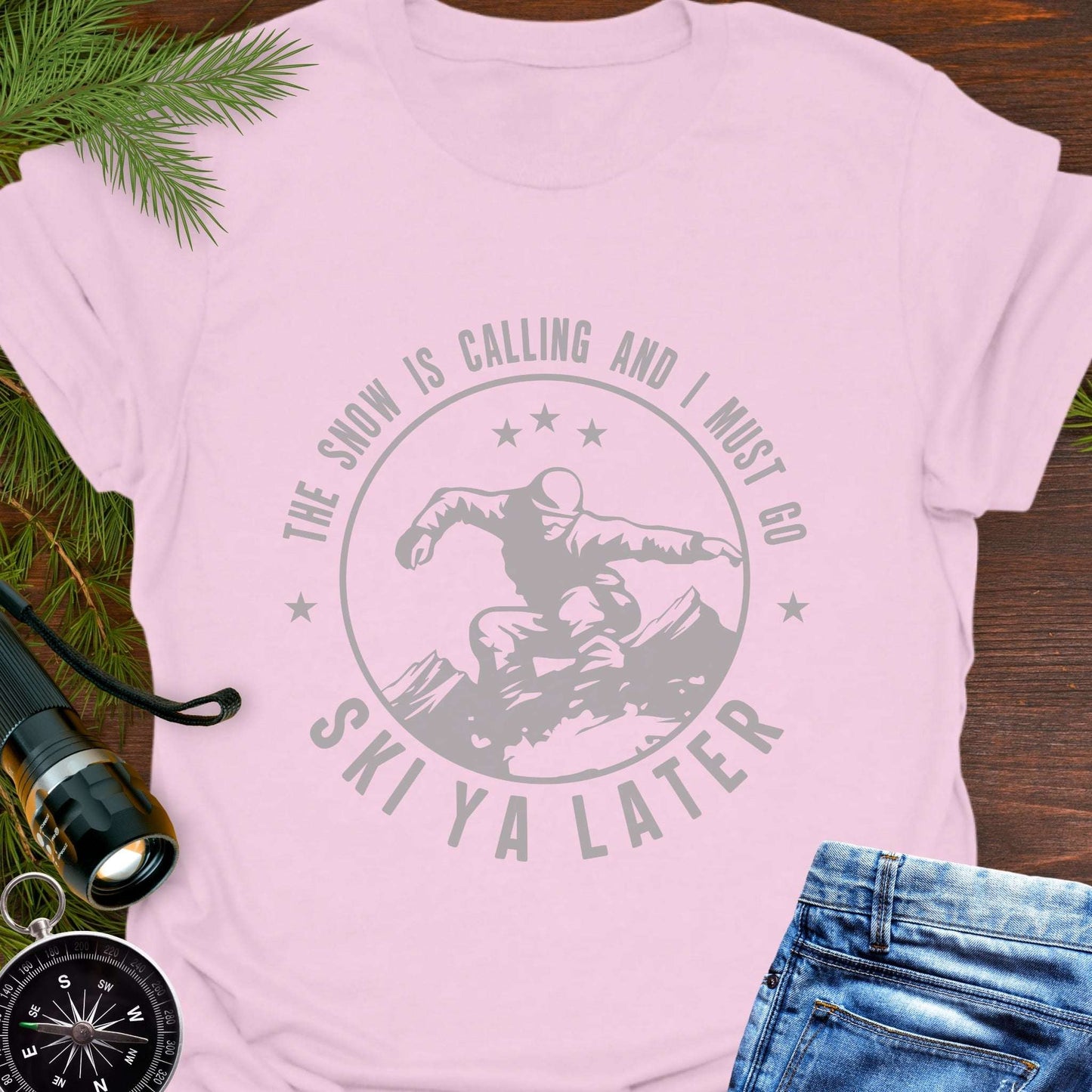 Pink t-shirt with skiing graphic and text Snow Is Calling – Ski Ya Later.