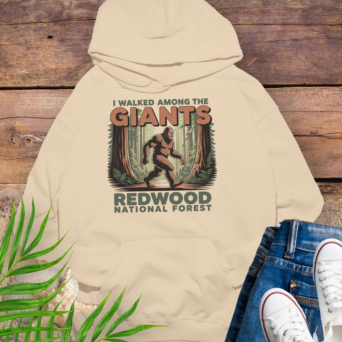 Beige hoodie with 'I Walked Among the Giants' Redwood National Forest design on a wooden background.