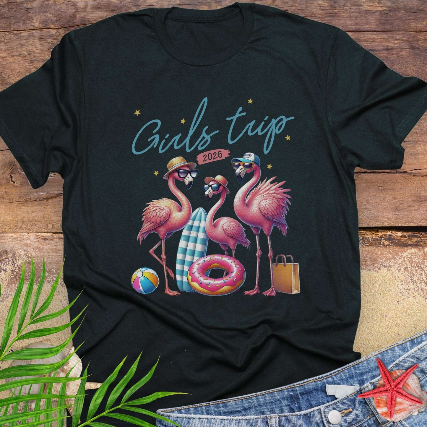 Black t-shirt with flamingo design and 'Girls trip 2026' text on a wooden surface.