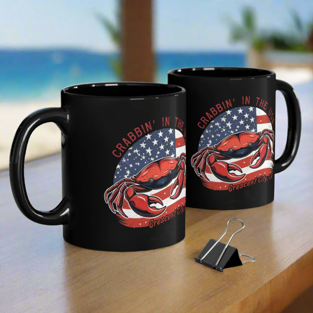 Two black mugs with a graphic design of a crab and American flag and Crescent City, CA.
