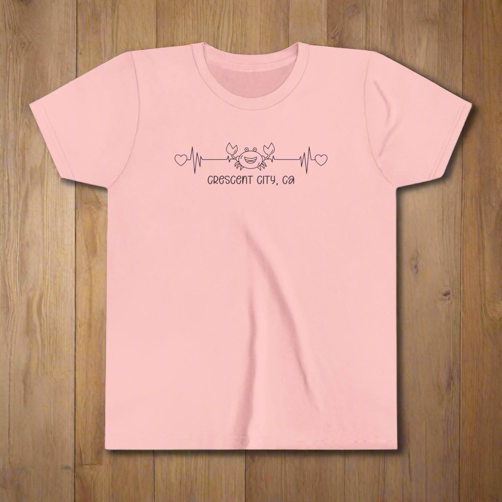 Pink Youth t-shirt with a smiley crab on a heartbeat line with hearts at both ends and “Crescent City, CA” underneath the design.