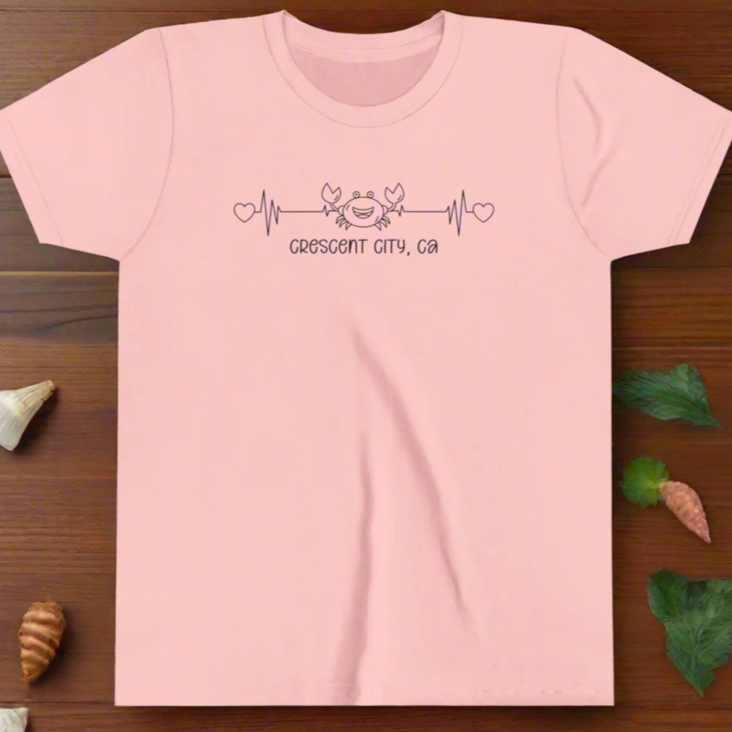 Pink Youth t-shirt with a smiley crab on a heartbeat line with hearts at both ends and “Crescent City, CA” underneath the design.