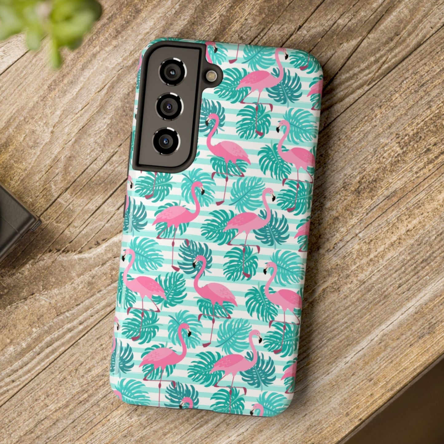 Phone case with flamingo and leaf pattern on a wooden surface