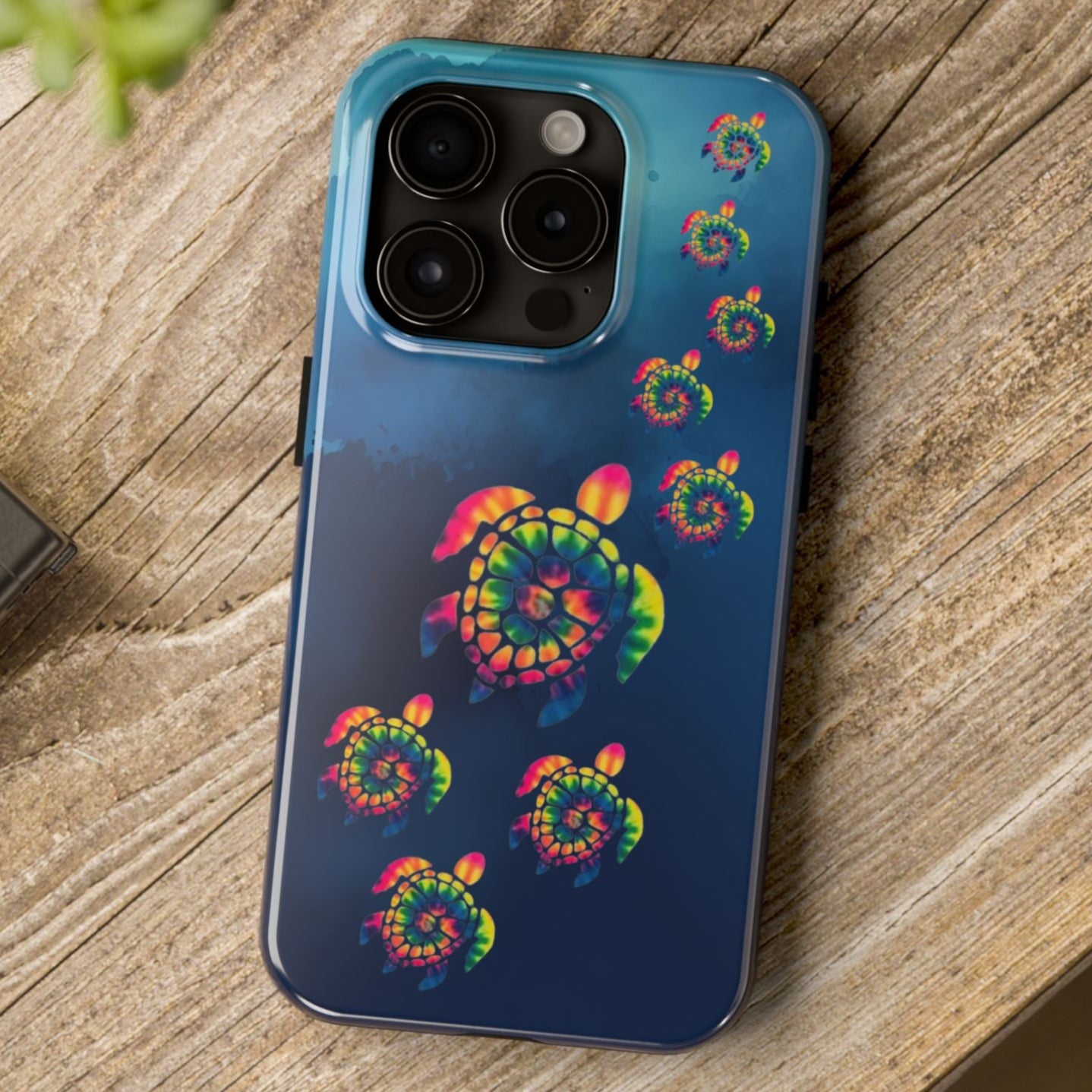 Phone case with colorful spiral design on a wooden surface next to a camera and plant.