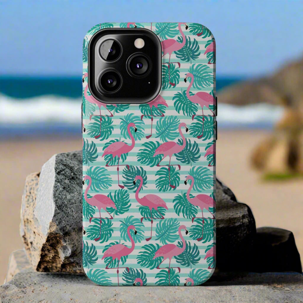 Phone case with flamingo and leaf pattern laying against rocks at the beach.