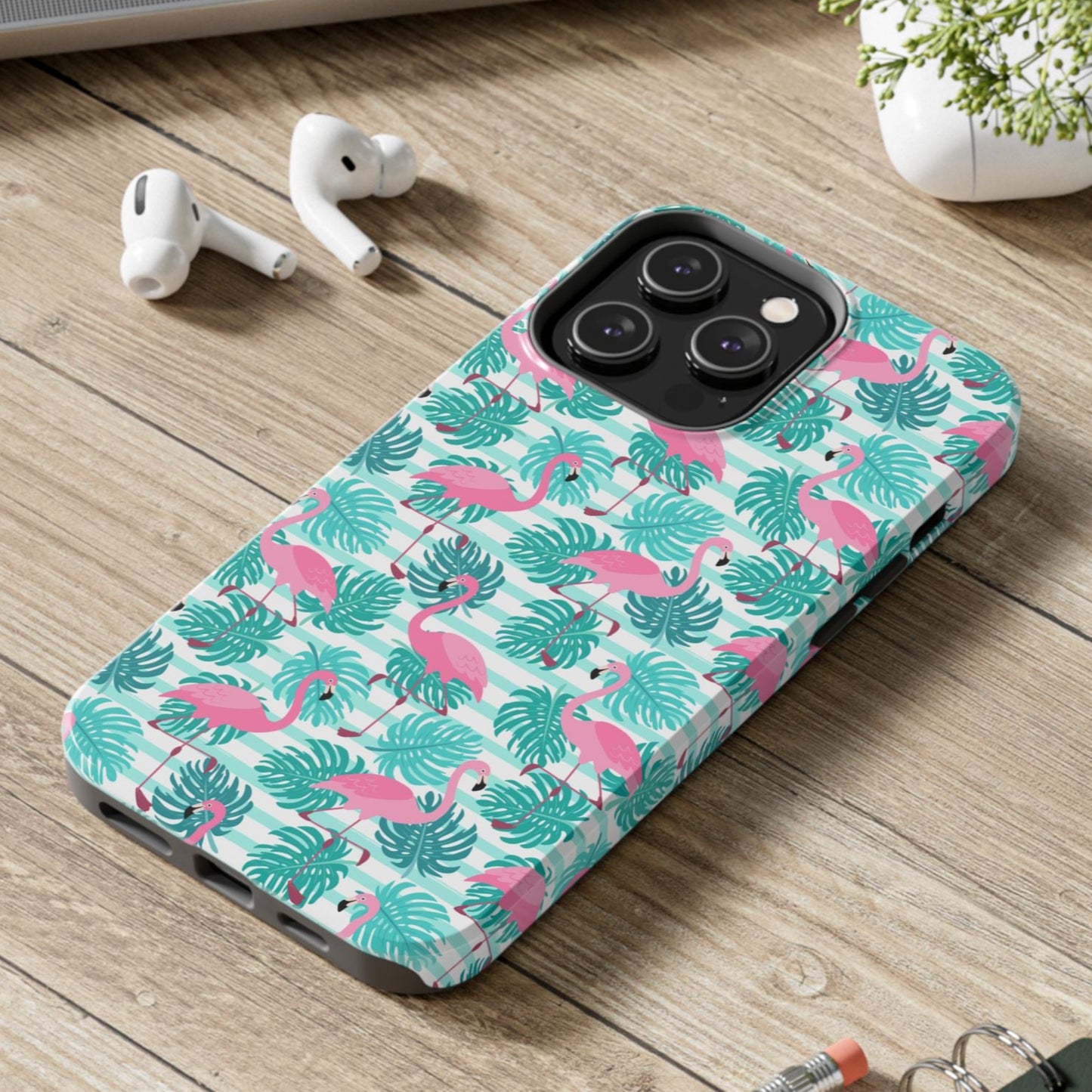 Phone case with flamingo pattern on a wooden surface with laptop, earbuds, and notebook.