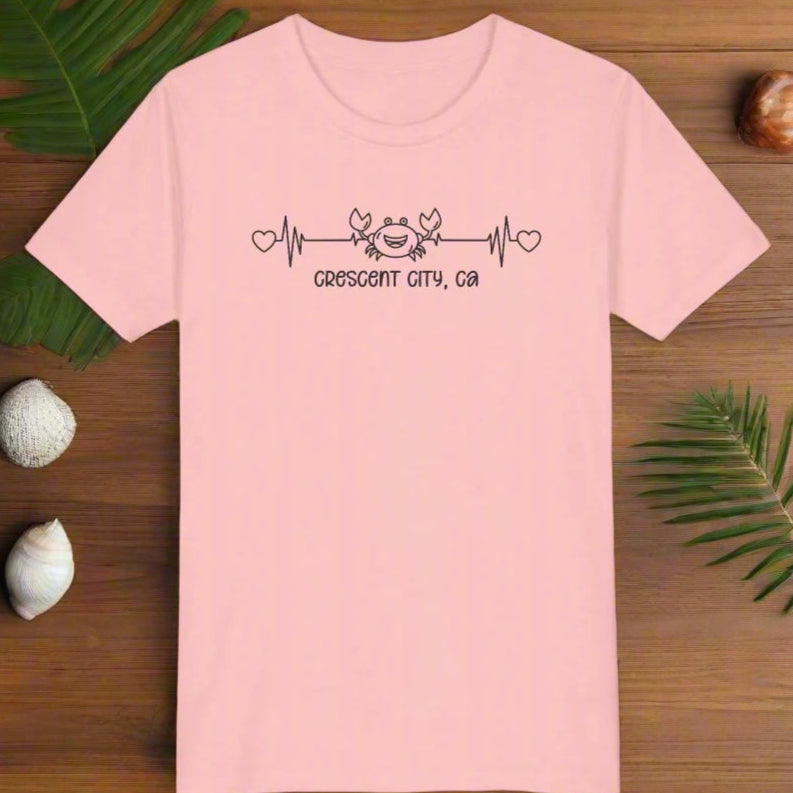 Pink Child t-shirt with a smiley crab on a heartbeat line with hearts at both ends and “Crescent City, CA” underneath the design.