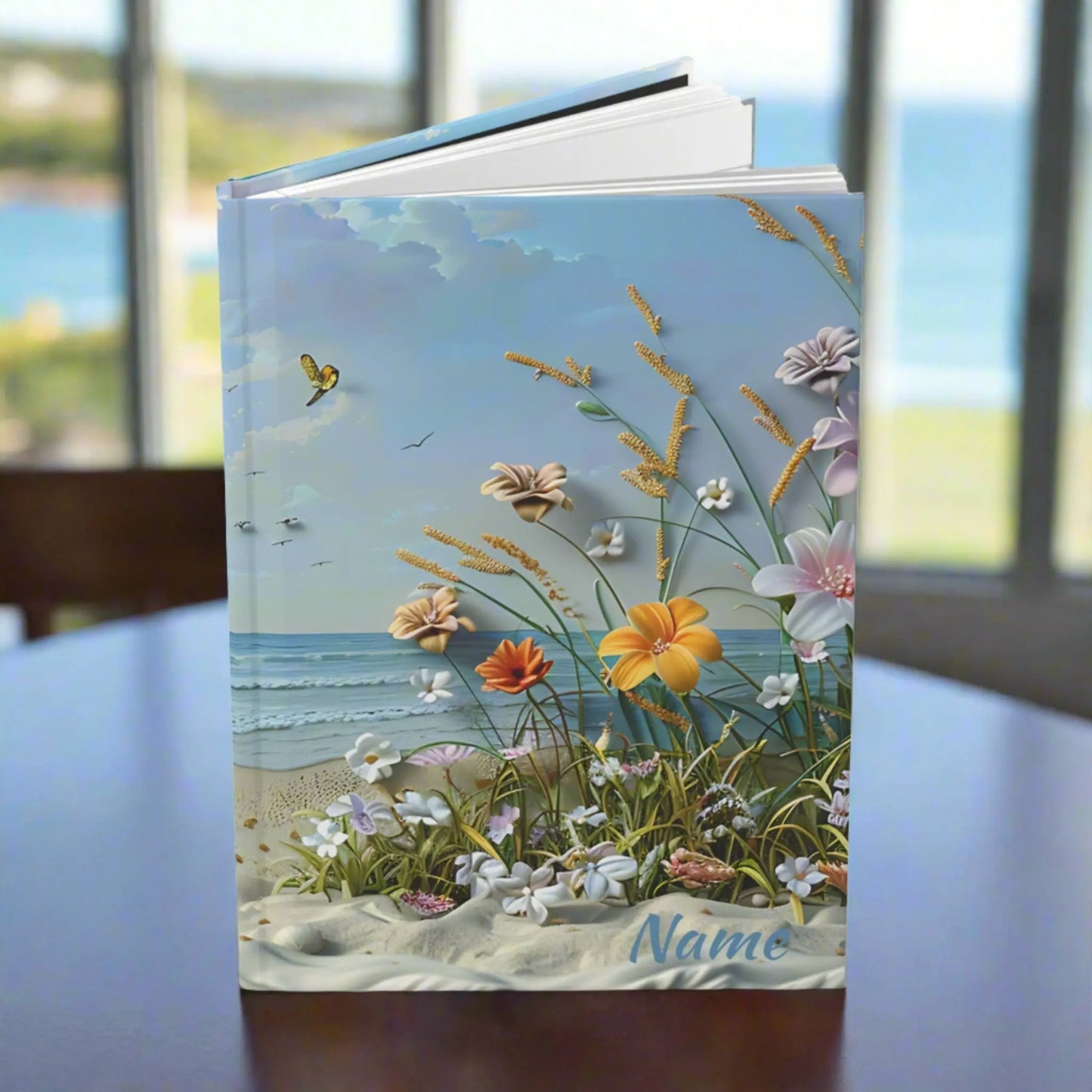 Hardcover journal with a scene of the beach with beach flowers and foliage laying personalized with the customers name.