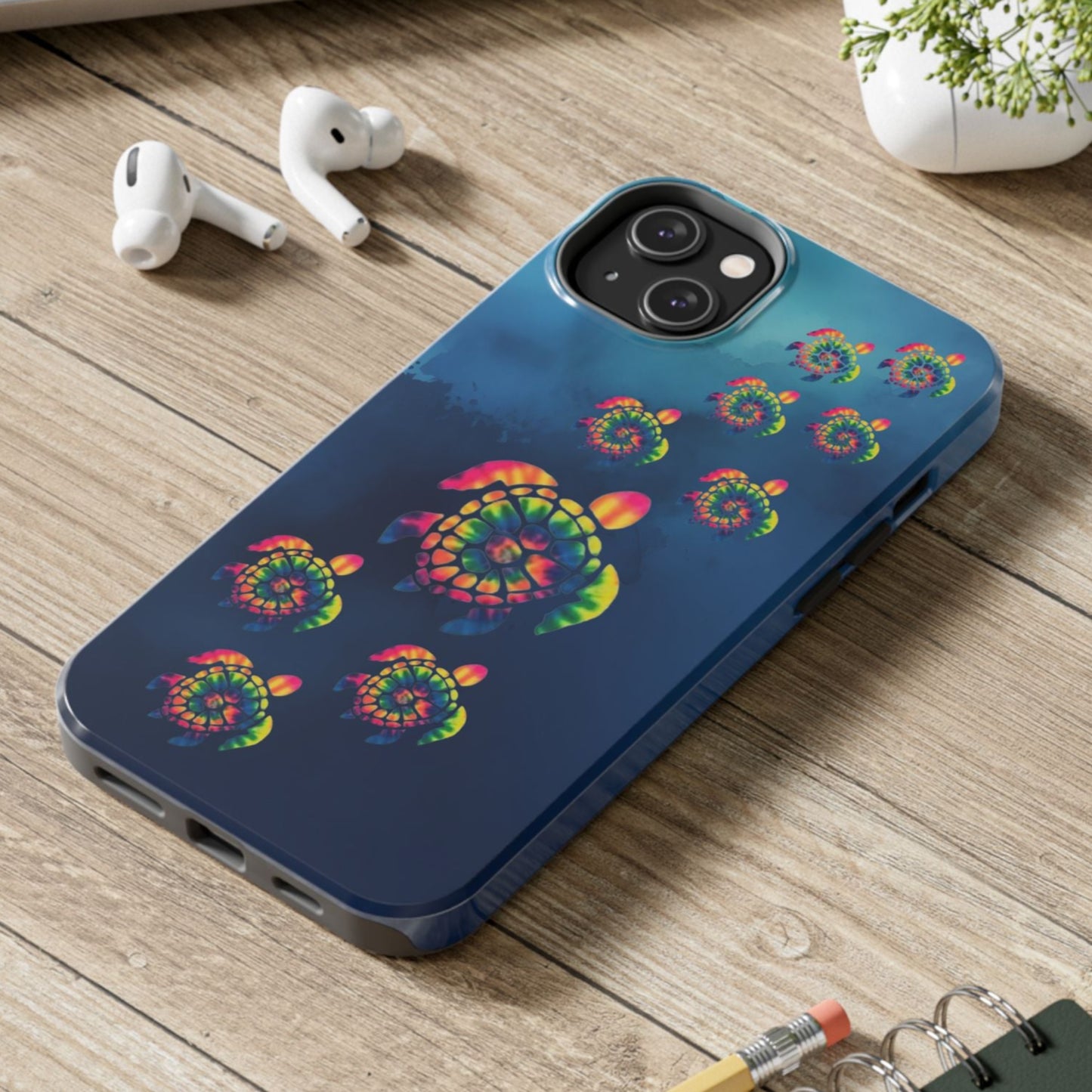 Phone case with colorful spiral design on a wooden surface with laptop, earbuds, and notebook.