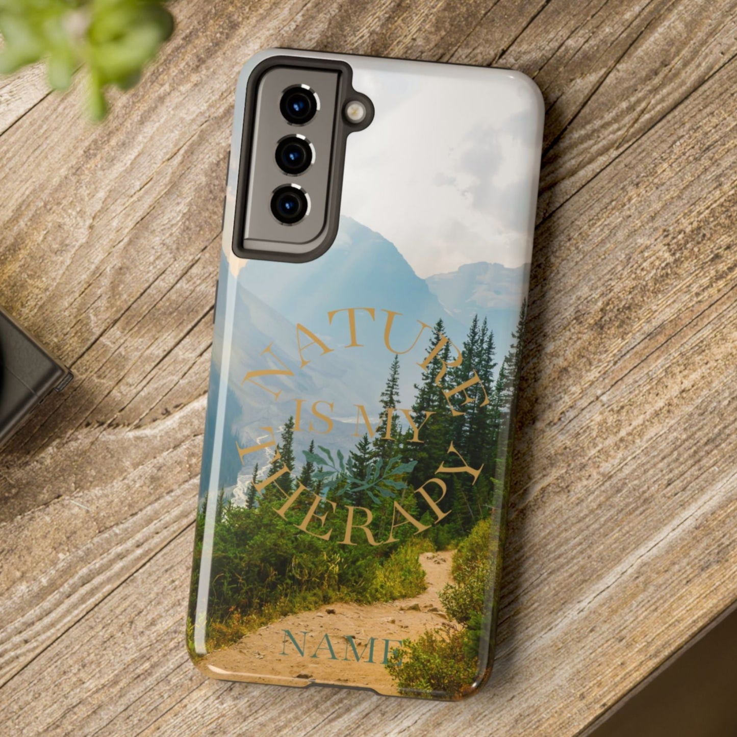 Phone case with nature design on a wooden surface next to a camera and plant.