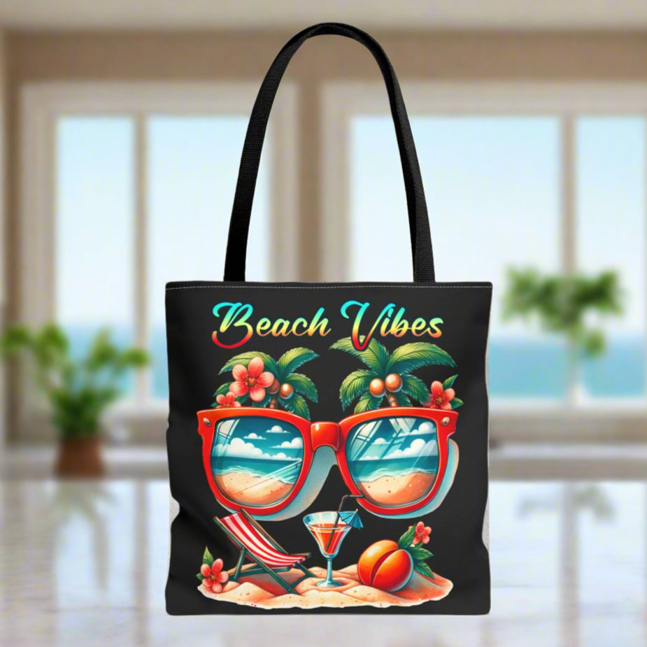 Black Tote bag featuring sunglasses with ocean and beach scene reflections, palm trees coming out of the glasses, a beach chair and cocktail on the sand, with the phrase "Beach Vibes" in a retro rainbow gradient font.