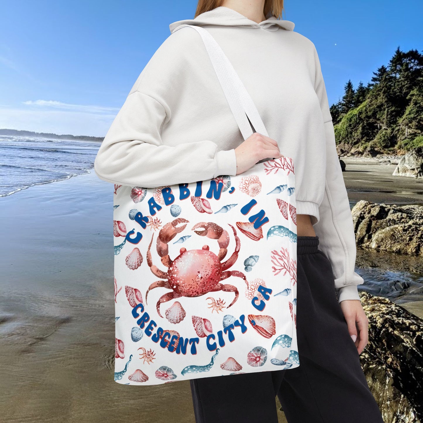 White 18" x 18" Tote bag featuring a crab surrounded by seashells and underwater life in blue and soft red tones with the phrase "Crabbin' in Crescent City, CA.