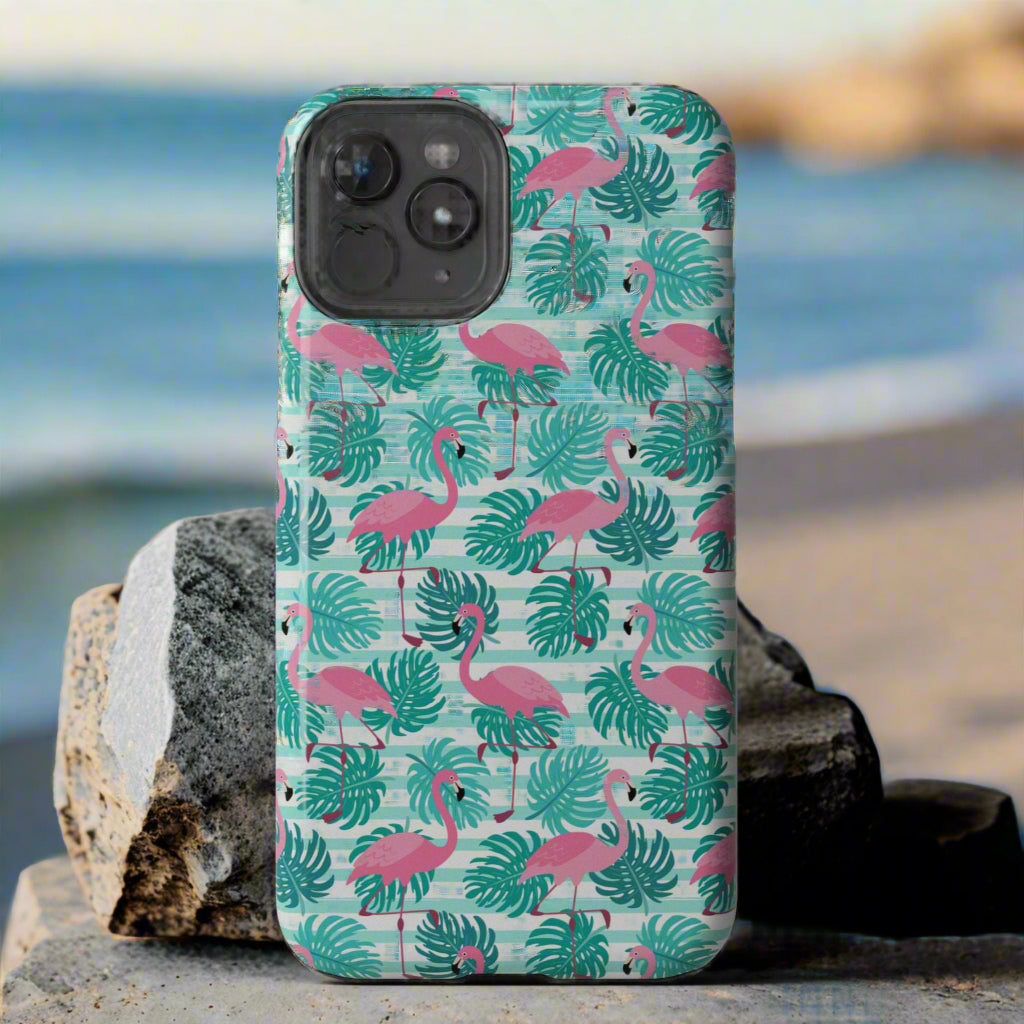 Phone case with flamingo and leaf pattern laying against rocks at the beach.