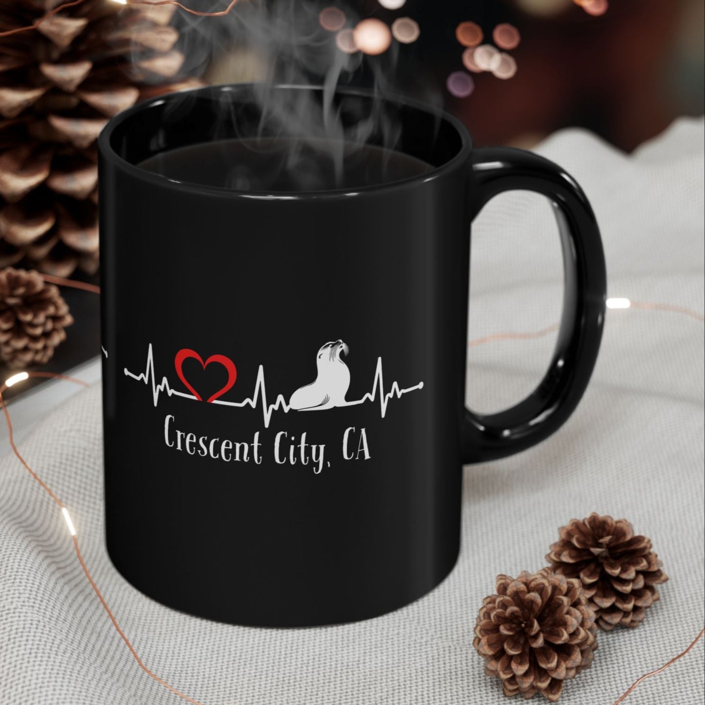 Black mug with a heart and paw print design, surrounded by decorative items on a table.