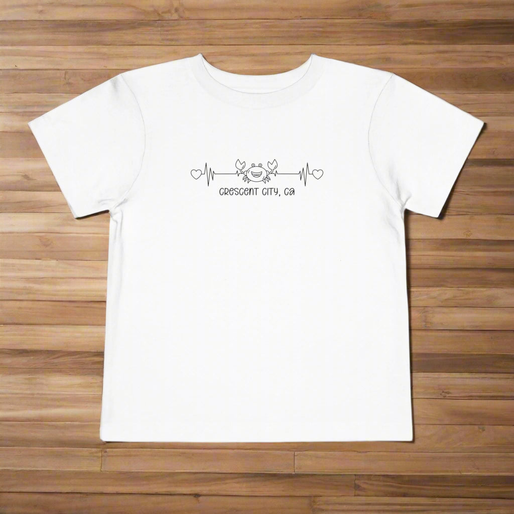 White Toddler t-shirt featuring a smiley crab on a heartbeat line with hearts at both ends and the text “Crescent City, CA” underneath.