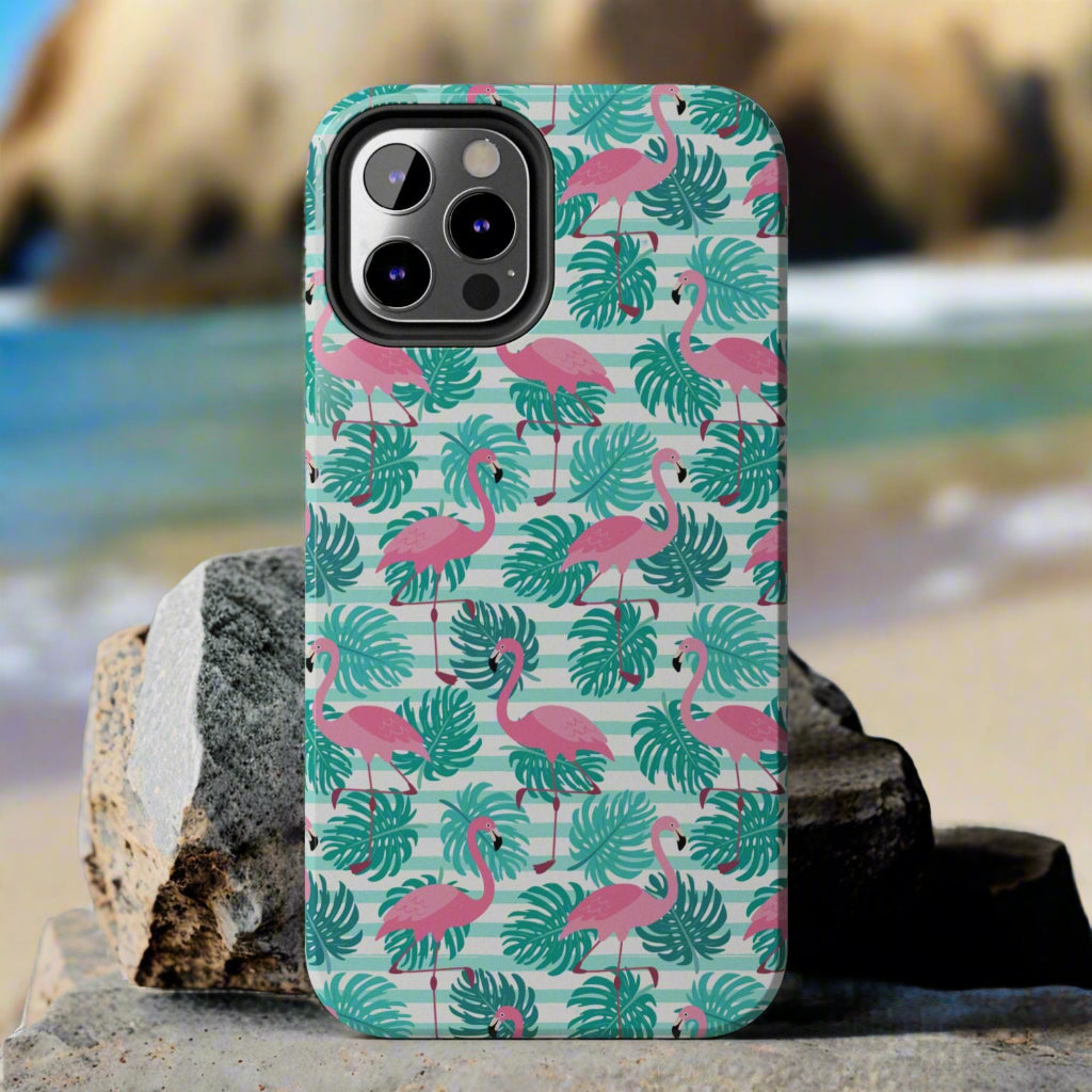 Phone case with flamingo and leaf pattern laying against rocks at the beach.