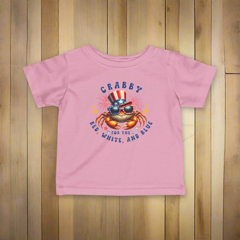 PInk Infant t-shirt with a crab wearing an American flag top hat surrounded by fireworks and seashells with the phrase “Crabby for the Red, White, and Blue.”