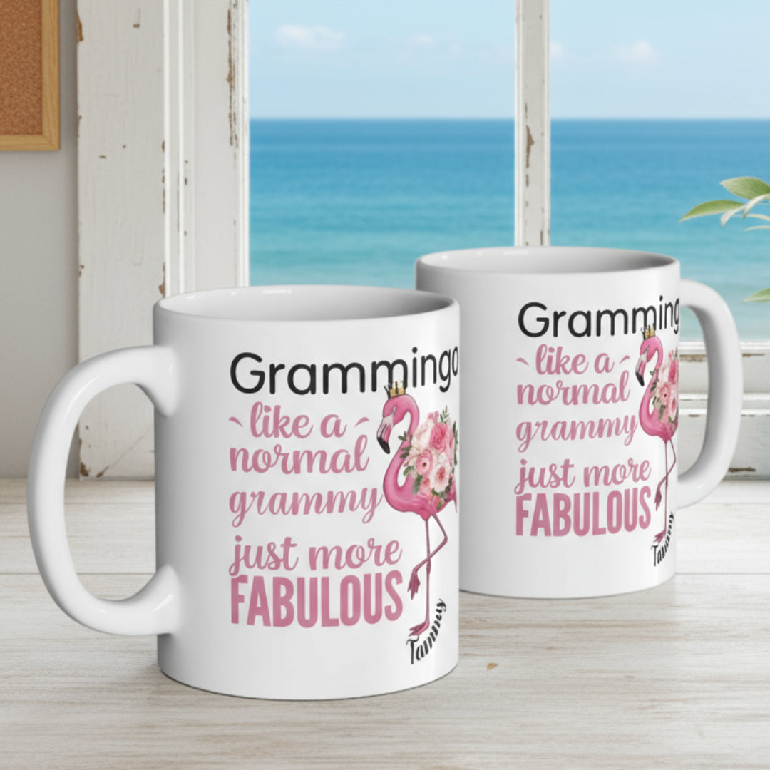 Ceramic coffee mug featuring a flamingo adorned with flowers and the text “Grammingo like a normal Grammy just more fabulous,” available with white, pink, or black handle options.
