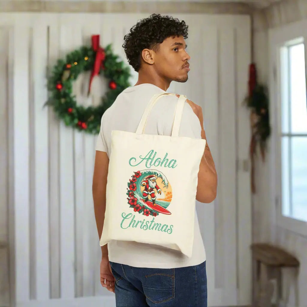 Our beige tote bag with Santa surfing a curl wave with red hibiscus flowers along the wave with a sunset behind him with the text Aloha Christmas.