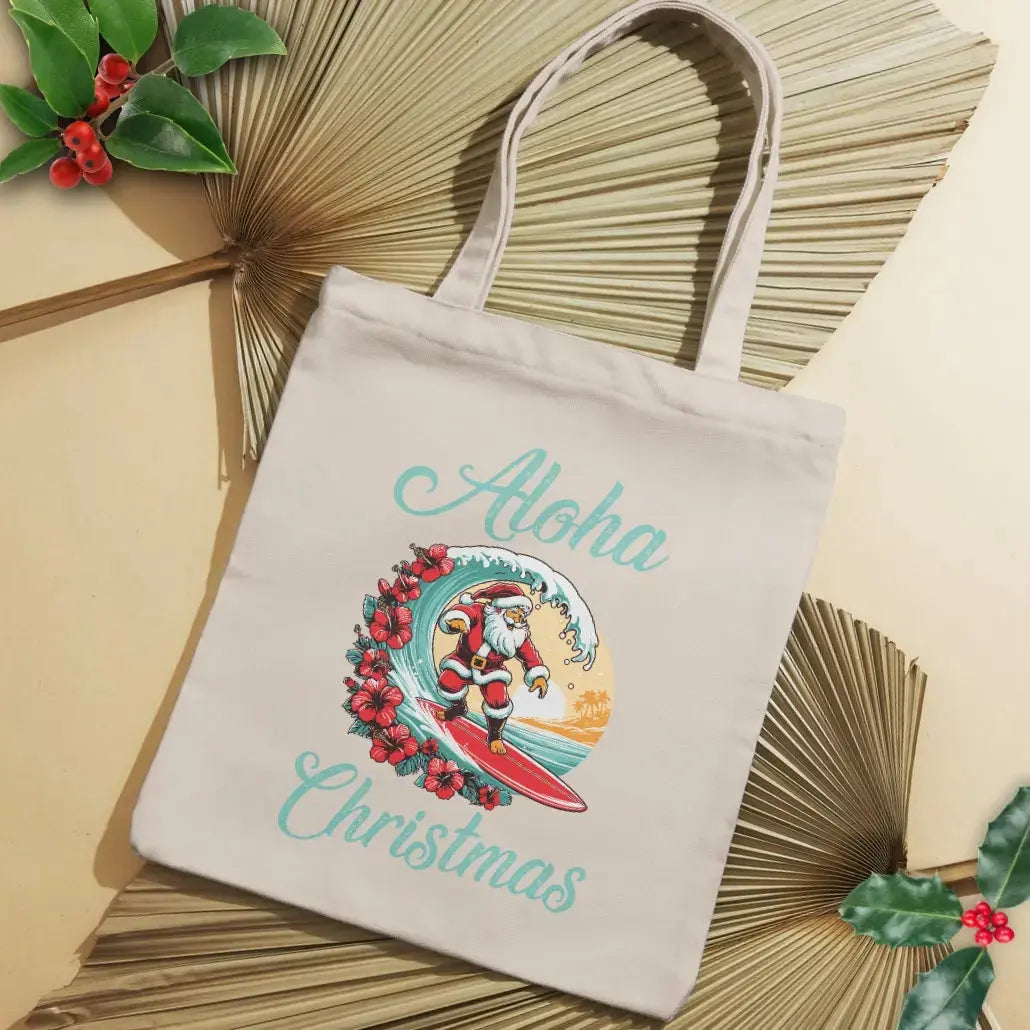 Our beige tote bag with Santa surfing a curl wave with red hibiscus flowers along the wave with a sunset behind him with the text Aloha Christmas.