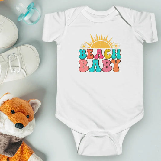 White short-sleeve baby bodysuit featuring 'Beach Baby' in a retro font with a sun over the text. Cute and stylish summer outfit for little beach lovers, perfect for beach days and coastal adventures.