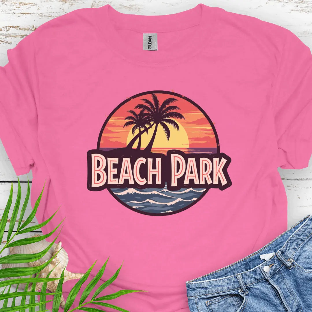 Azalea T-shirt with a vintage-style logo inspired by Jurassic Park, but with a beach theme featuring a circular emblem with a bold, retro font spelling 'BEACH PARK' in the center. The dinosaur silhouette is replaced with a tropical scene of palm trees.