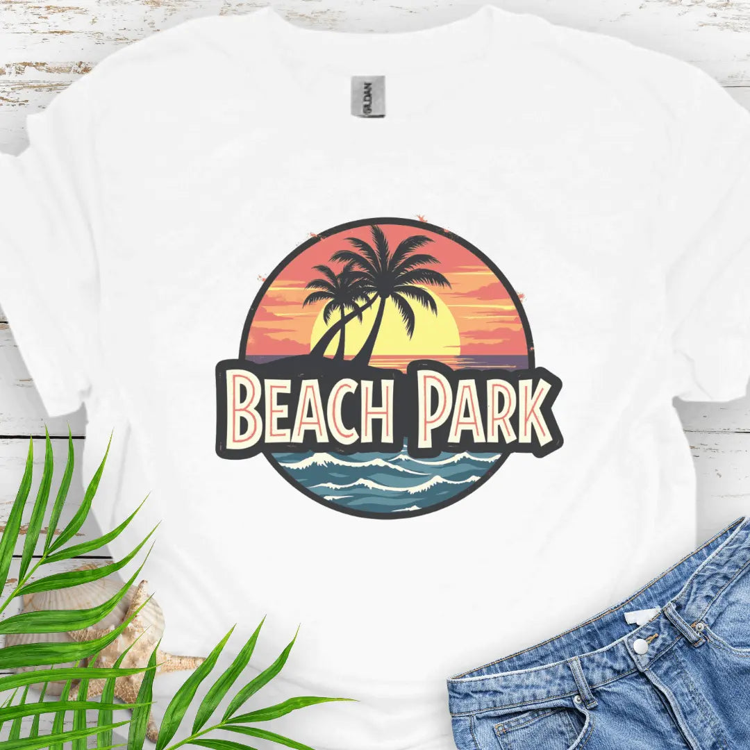 White T-shirt with a vintage-style logo inspired by Jurassic Park, but with a beach theme featuring a circular emblem with a bold, retro font spelling 'BEACH PARK' in the center. The dinosaur silhouette is replaced with a tropical scene of palm trees.