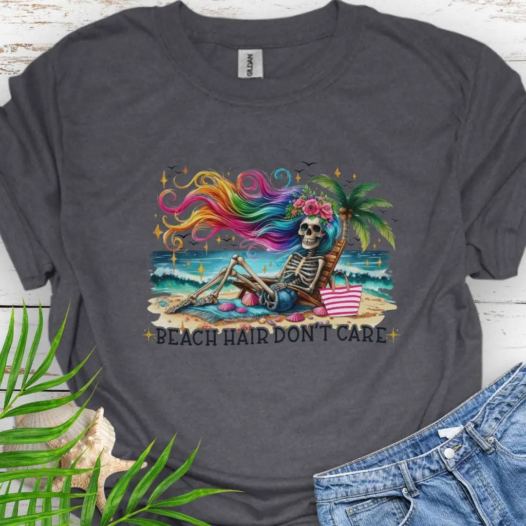 Dark Heather T-shirt with a skeleton with rainbow hair flowing in the wind laying on a beach chair at the ocean that says Beach Hair Don't Care.