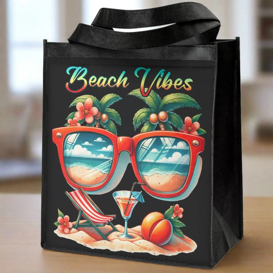Black tote bag sitting on a dining room table with the words Beach Vibes over a beach scene with sunglasses that show the ocean in the lenses.