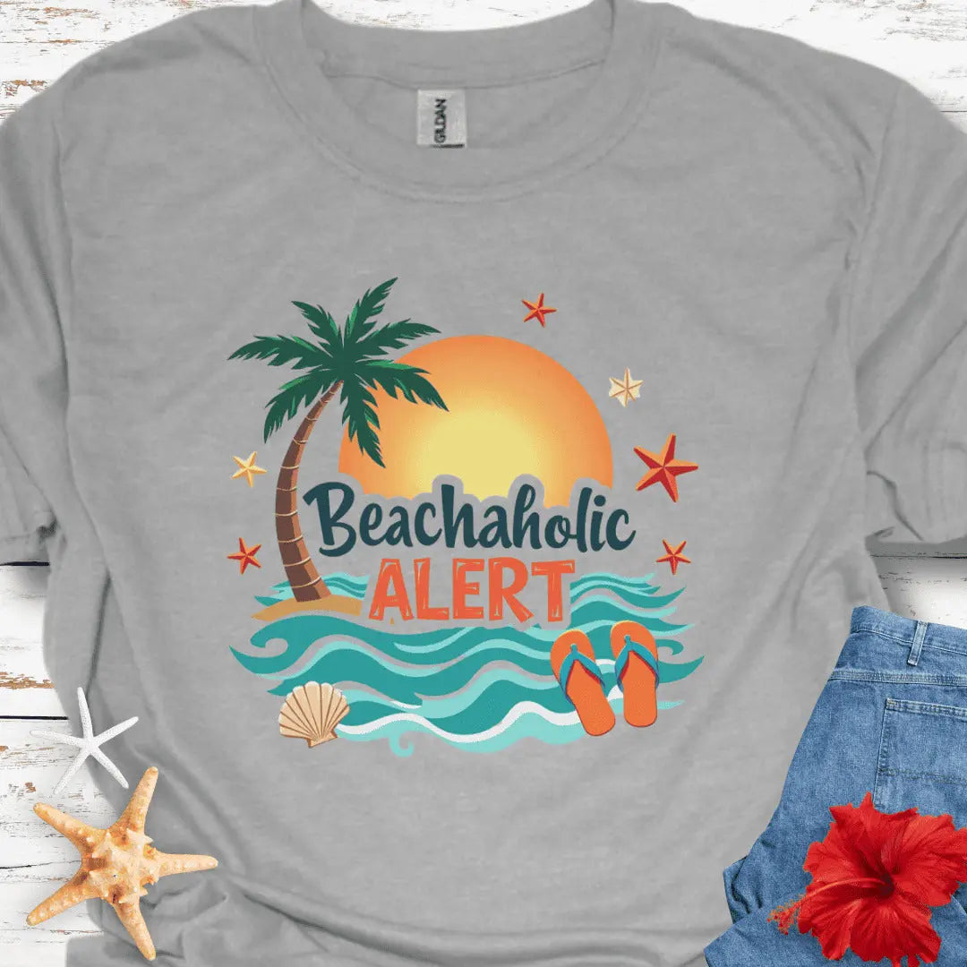 Gray unisex t-shirt with “Beachaholic Alert” text and colorful graphic of palm tree, sunset, waves, starfish, and flip-flops.