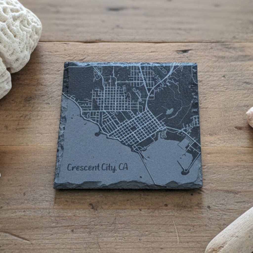 Slate coaster with engraved map of Crescent City, CA on a wooden surface.