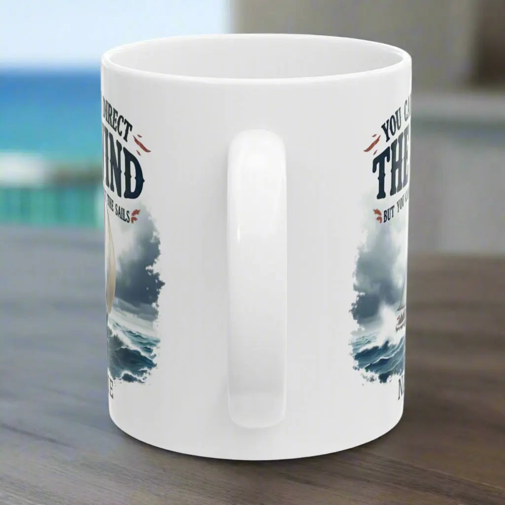 Side view of a white 11 oz. mug with a sailboat on the ocean with text 'You Can't Direct the Wind But You Can Adjust the Sails' with personalized name.