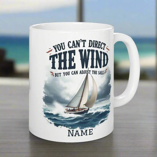 A white 11 oz. mug with a sailboat on the ocean with text 'You Can't Direct the Wind But You Can Adjust the Sails' with personalized name.