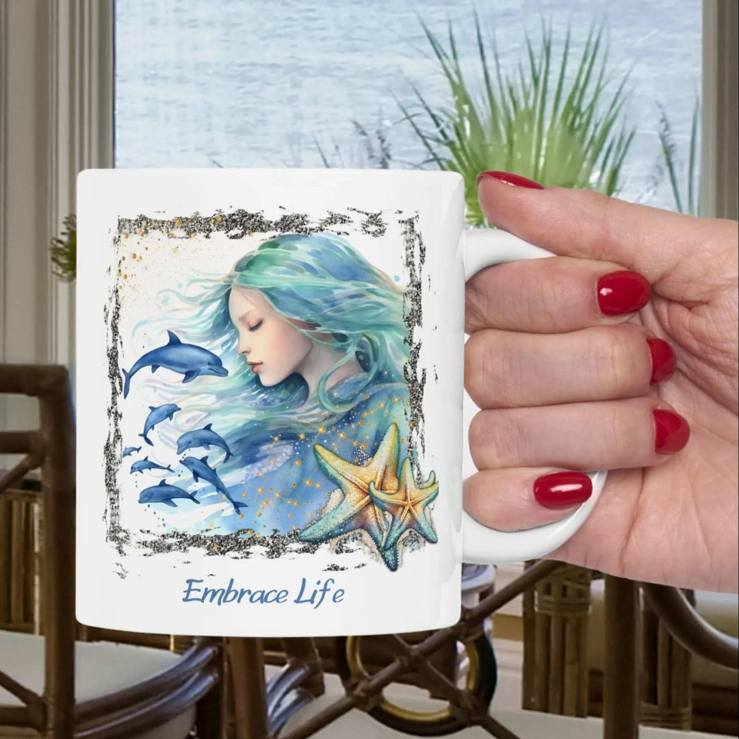White 11 oz Ceramic Mug with a mermaid and swimming dolphins gives a mystical and positive vibe with the text Embrace Life - ideal for those who love the beach and marine life!