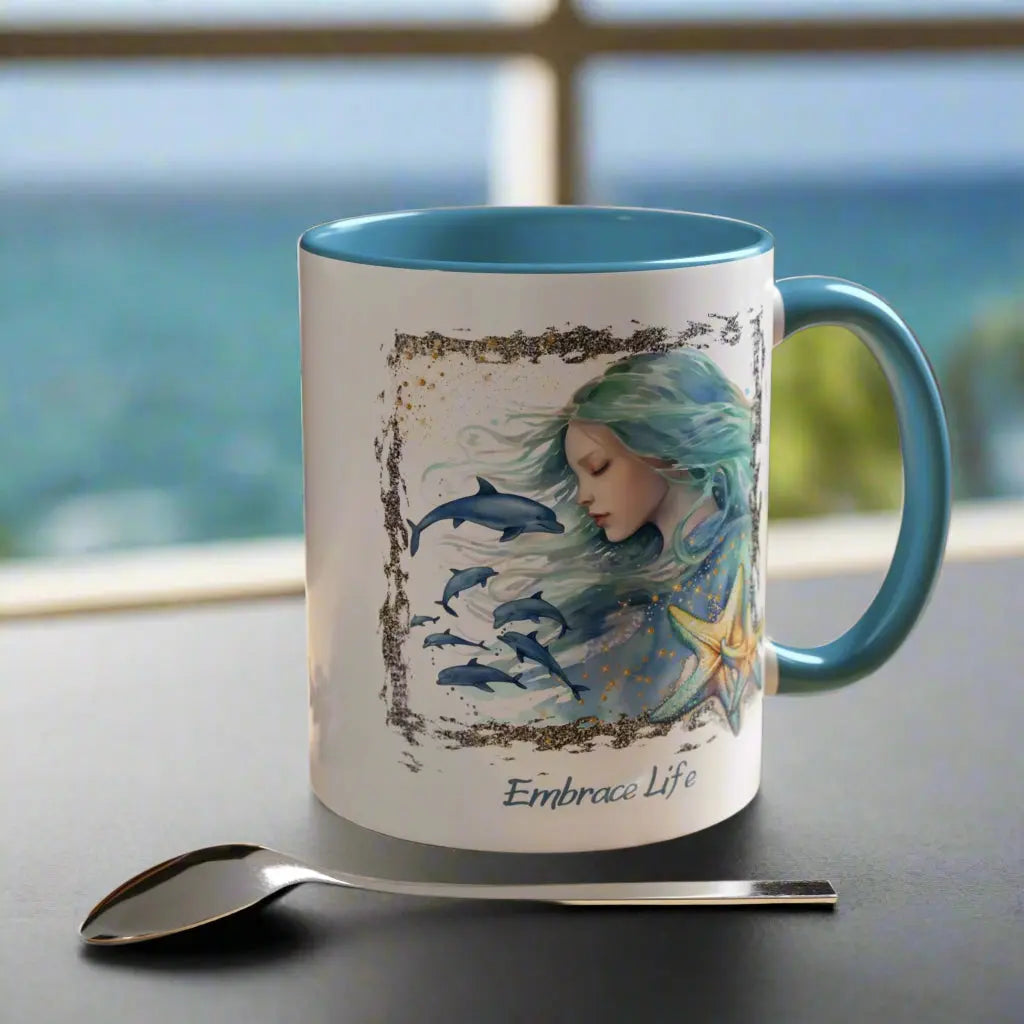 White 11 oz Ceramic Mug with light blue handle and inside with a mermaid and swimming dolphins gives a mystical and positive vibe with the text Embrace Life - ideal for those who love the beach and marine life!