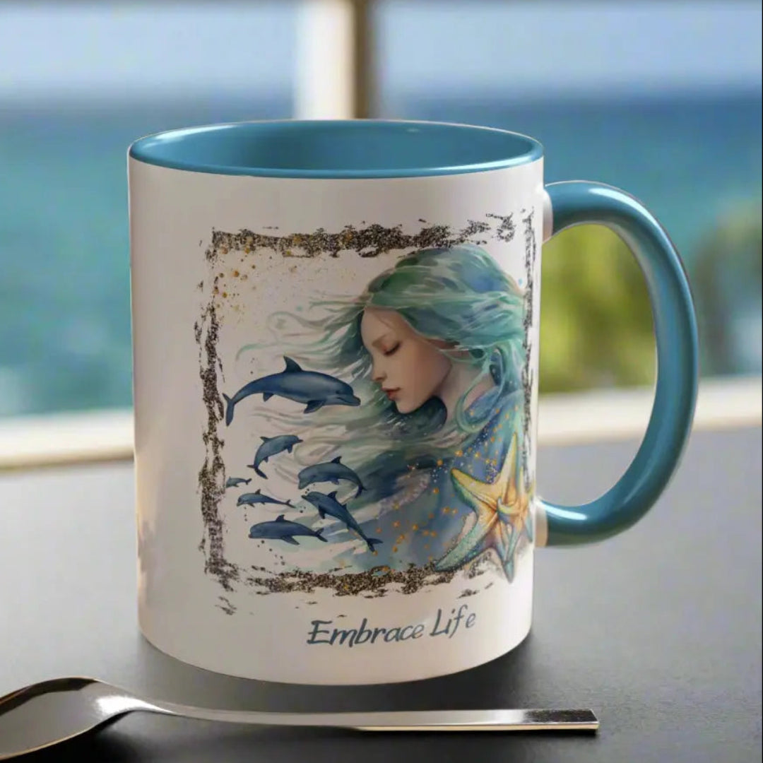 White 11 oz Ceramic Mug with light blue handle and inside with a mermaid and swimming dolphins gives a mystical and positive vibe with the text Embrace Life - ideal for those who love the beach and marine life!