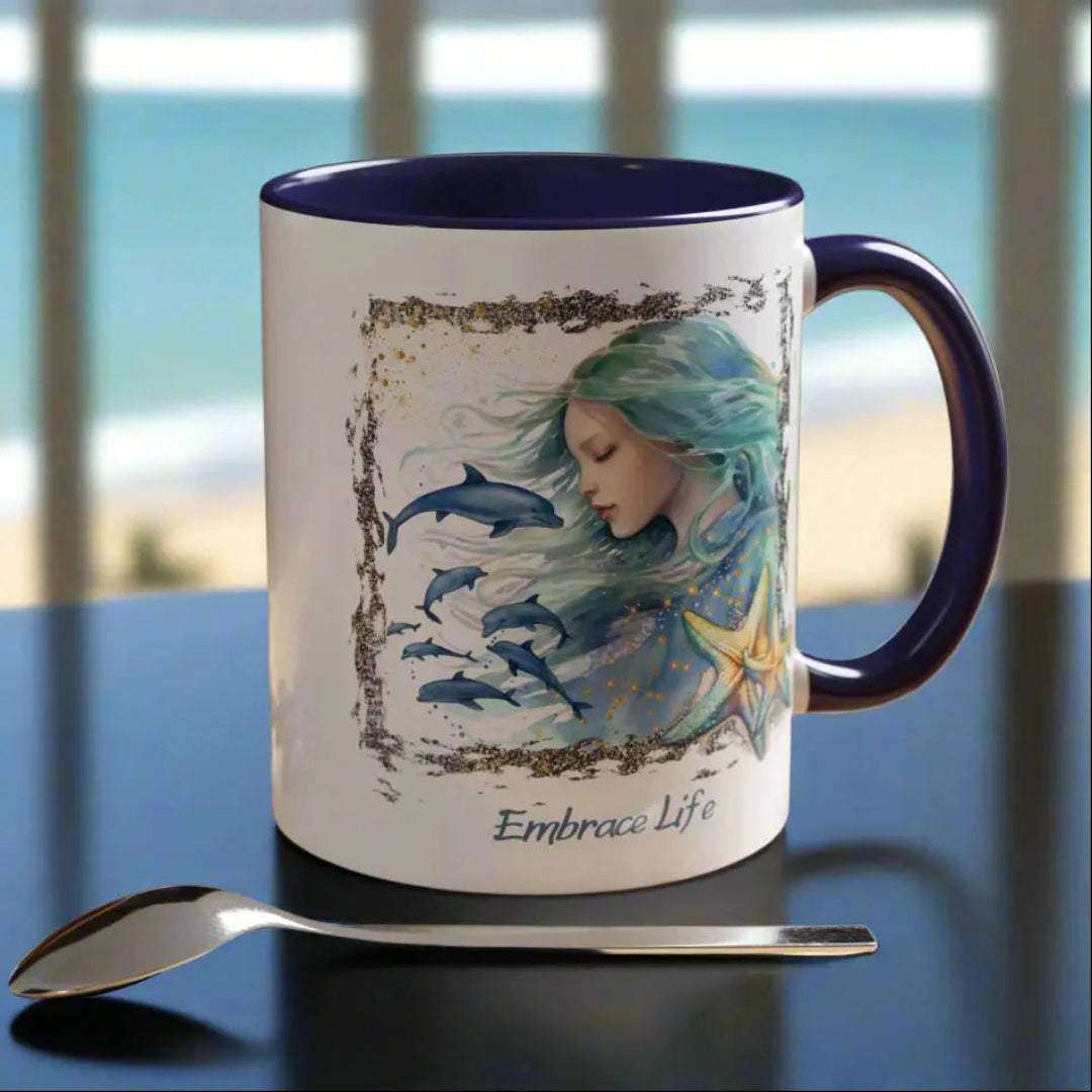 White 11 oz Ceramic Mug with blue handle and inside with a mermaid and swimming dolphins gives a mystical and positive vibe with the text Embrace Life - ideal for those who love the beach and marine life!