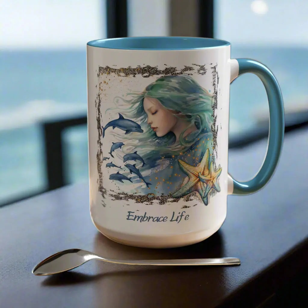 White 15 oz Ceramic Mug with light blue handle and inside with a mermaid and swimming dolphins gives a mystical and positive vibe with the text Embrace Life - ideal for those who love the beach and marine life!