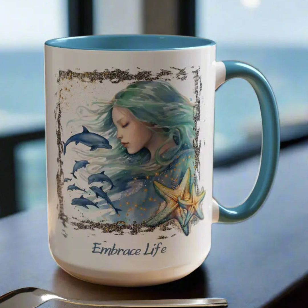 White 15 oz Ceramic Mug with light blue handle and inside with a mermaid and swimming dolphins gives a mystical and positive vibe with the text Embrace Life - ideal for those who love the beach and marine life!