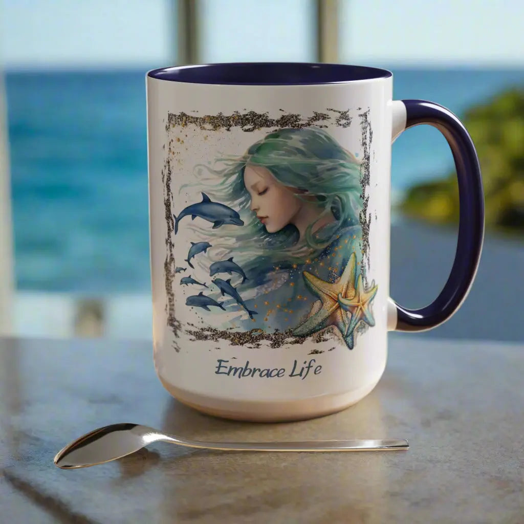White 15 oz Ceramic Mug with blue handle and inside with a mermaid and swimming dolphins gives a mystical and positive vibe with the text Embrace Life - ideal for those who love the beach and marine life!