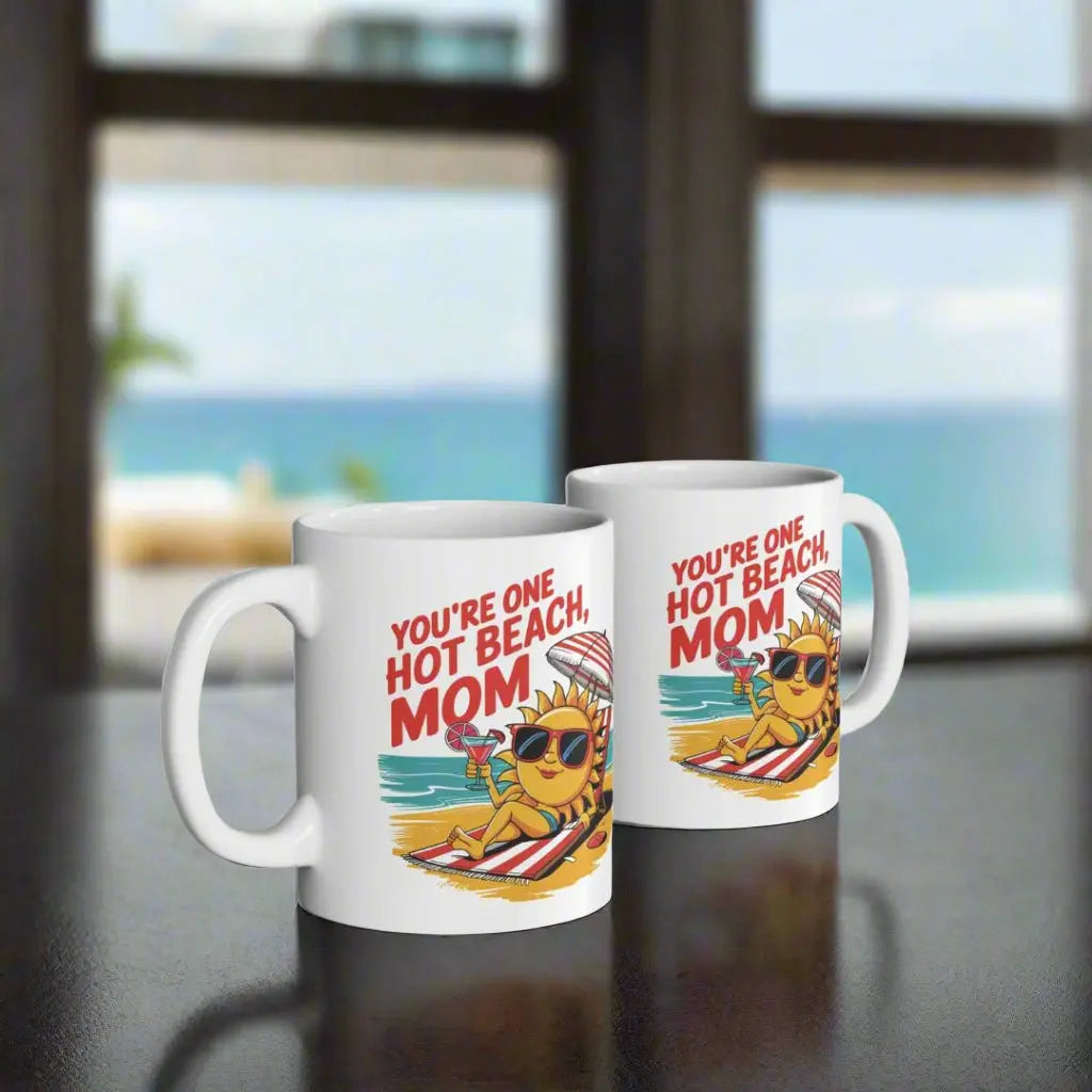 Two white 11 oz mugs with a sexy sun laying on a beach towel holding a drink on the beach that says You're One Hot Beach Mom.