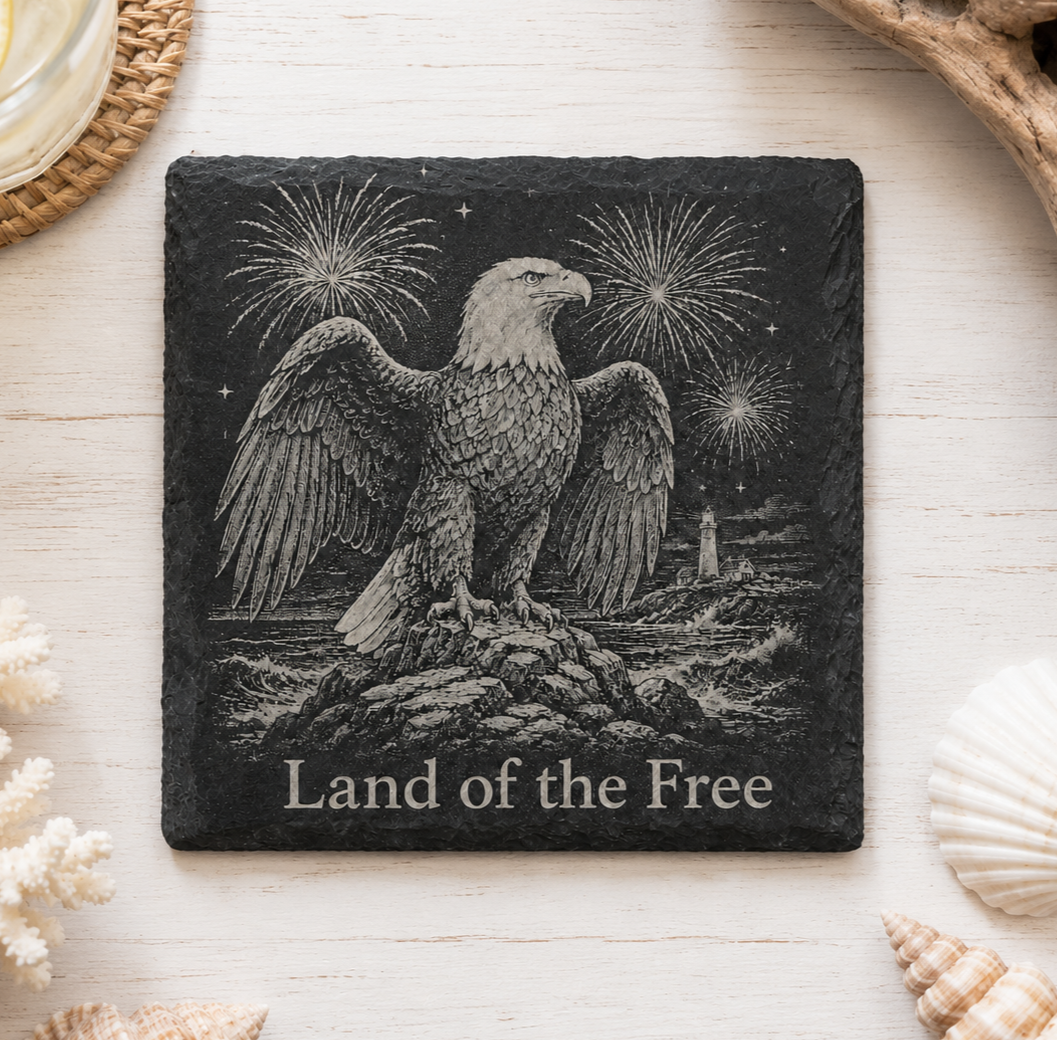Laser engraved natural slate coaster featuring a bald eagle, fireworks, lighthouse, and "Land of the Free" with protective padded feet.