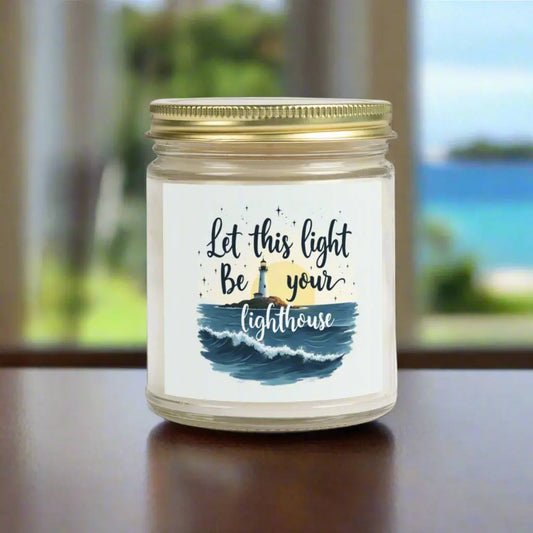 A 9 oz clear jar scented candle featuring a lighthouse with the sun and the phrase 'Let this Light Be Your Lighthouse.' A calming and inspirational candle, perfect for coastal decor.
