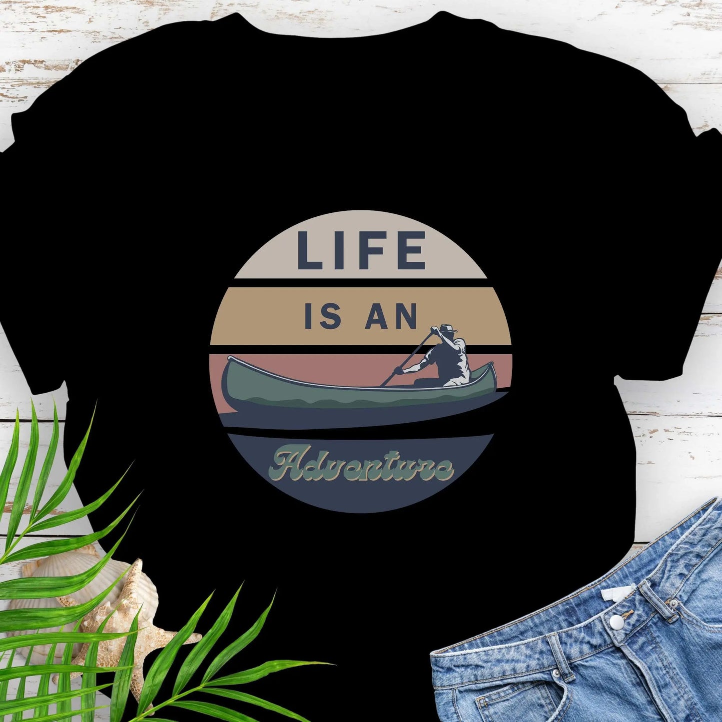 Black t-shirt featuring a retro sunset design with a man paddling a canoe and the phrase "Life is an Adventure" in bold, vintage-style font. Perfect for outdoor lovers, kayakers, and adventure seekers.