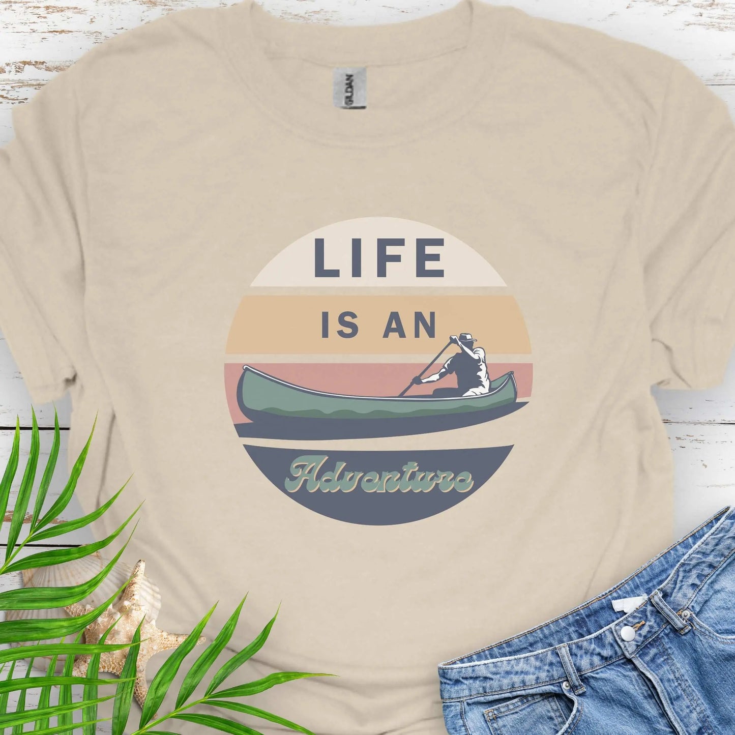 Natural t-shirt featuring a retro sunset design with a man paddling a canoe and the phrase "Life is an Adventure" in bold, vintage-style font. Perfect for outdoor lovers, kayakers, and adventure seekers.