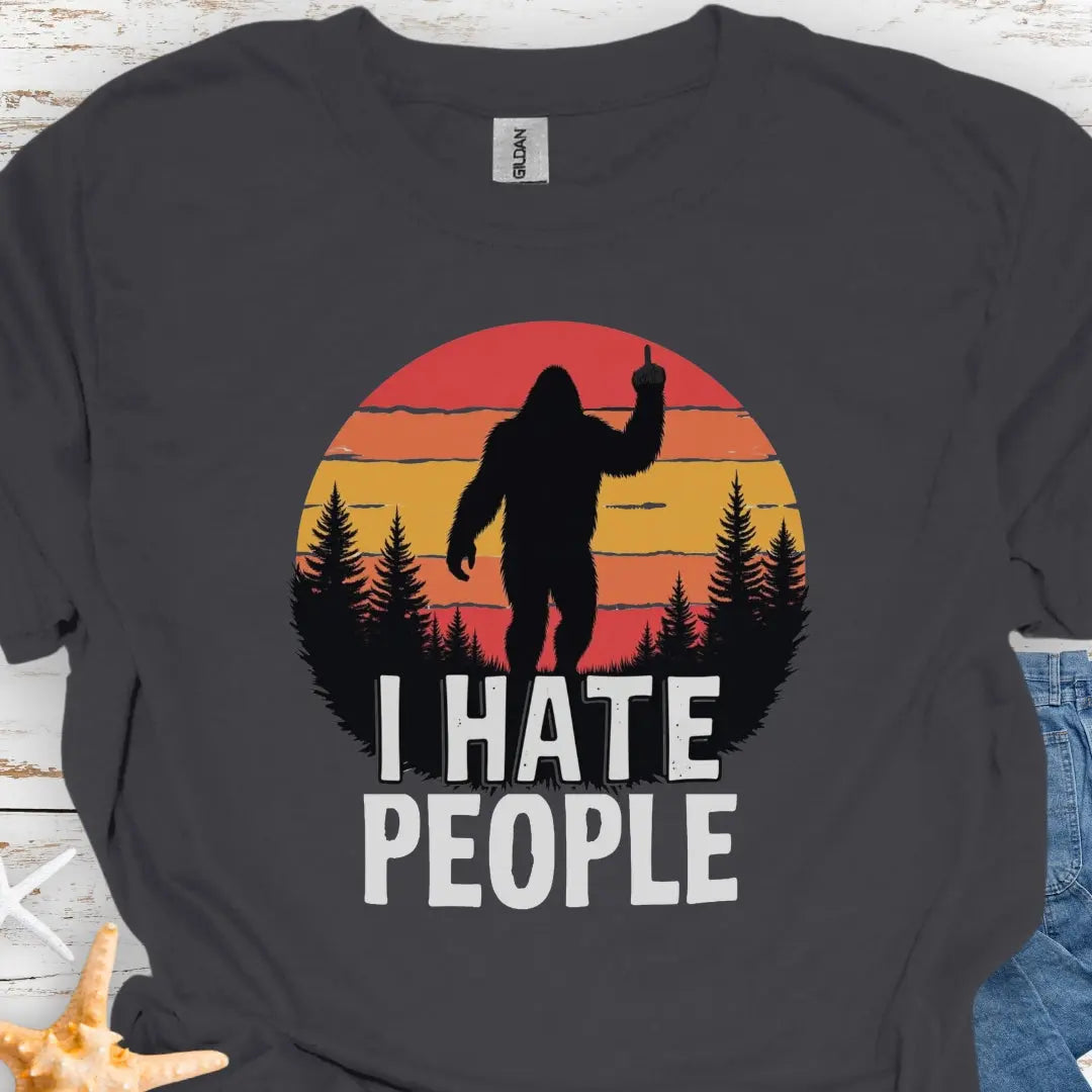 Charcoal t-shirt with sasquatch holding up middle finger walking into retro sunset with black forest with text I hate people.