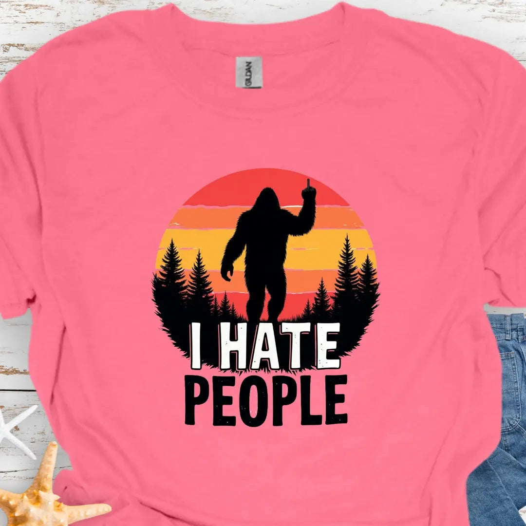 Coral Silk t-shirt with sasquatch holding up middle finger walking into retro sunset with black forest with text I hate people.