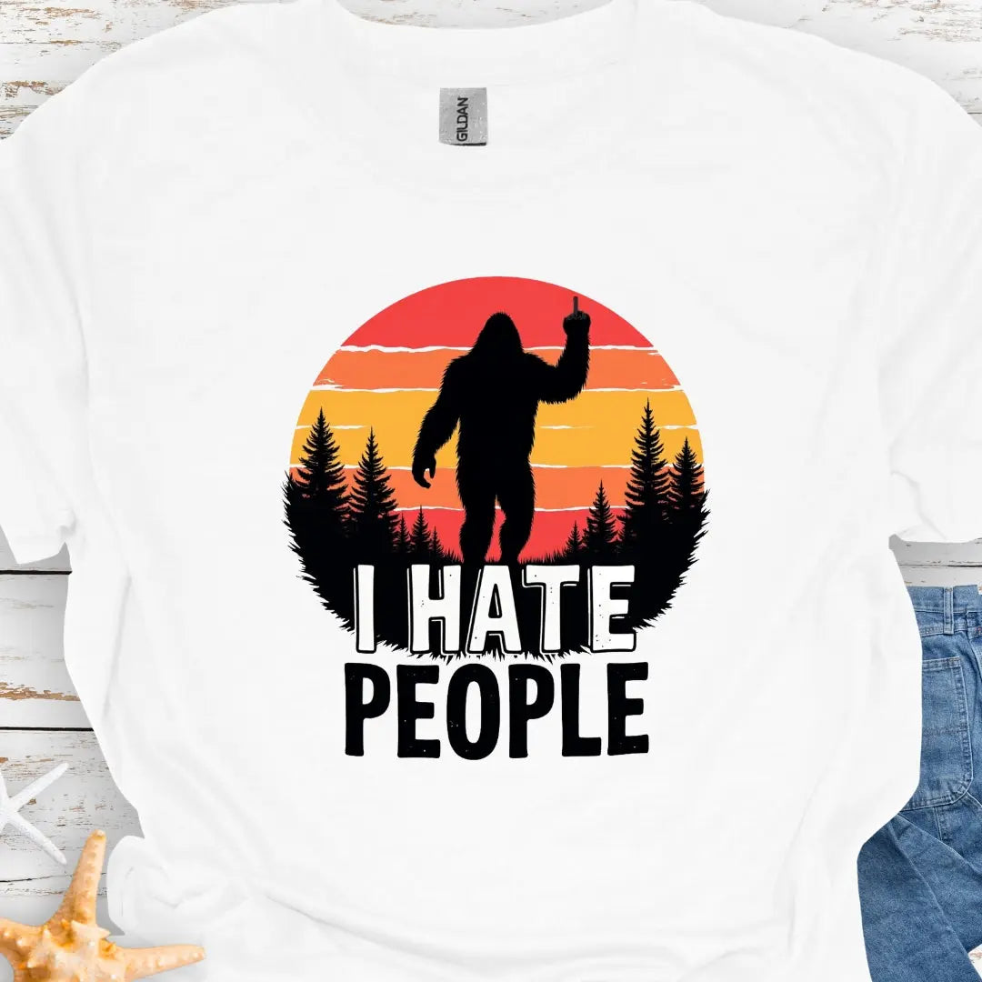 White t-shirt with sasquatch holding up middle finger walking into retro sunset with black forest with text I hate people.