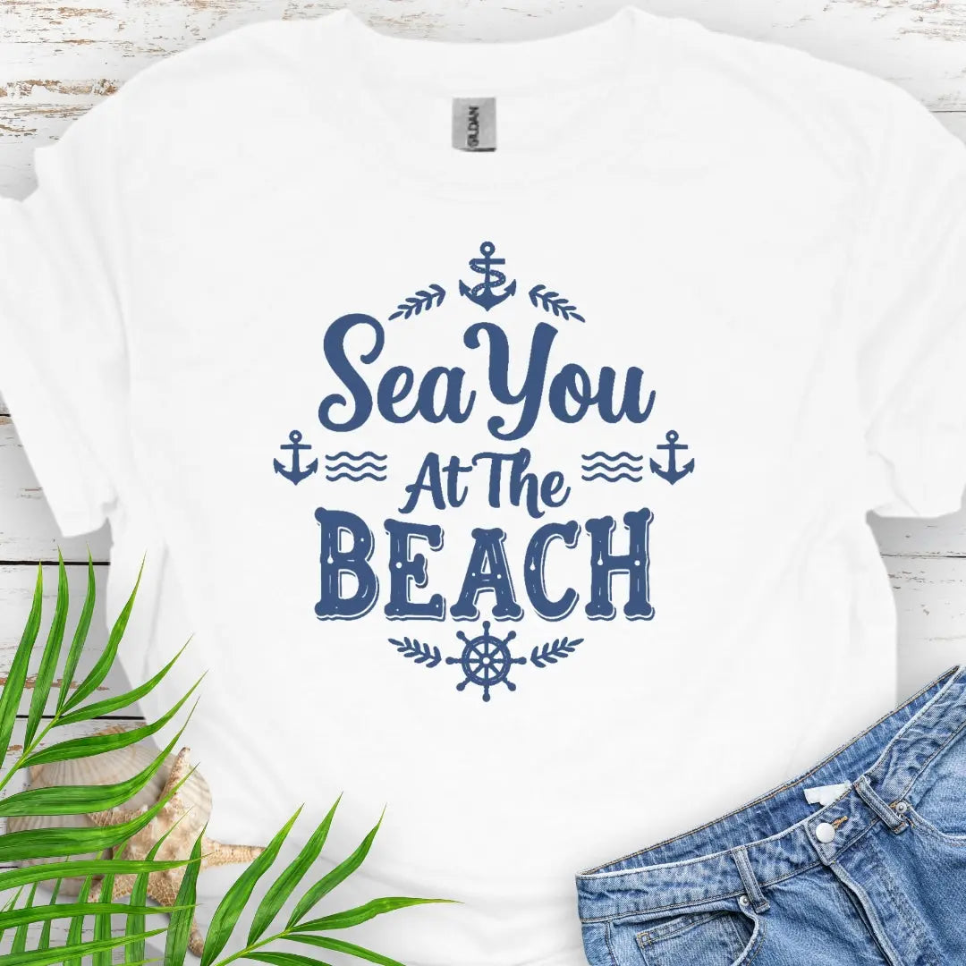 A white unisex t-shirt with white nautical graphics and the text “Sea You at the Beach” surrounded by anchors, waves, and ship wheel.
