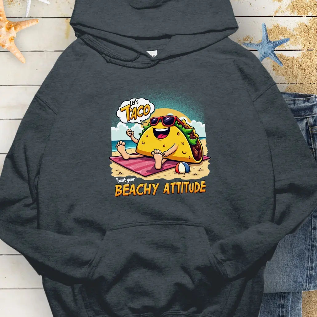 Dark Heather hoodie with a taco wearing sunglasses laying on a beach towel on the beach with the text Let's Taco 'bout your Beachy Attitude.